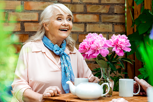 selective focus of happy retired woman smiling near pink flowers