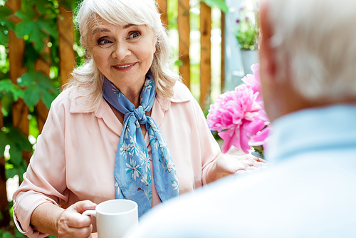 selective focus of happy senior woman looking at husband while holding cup