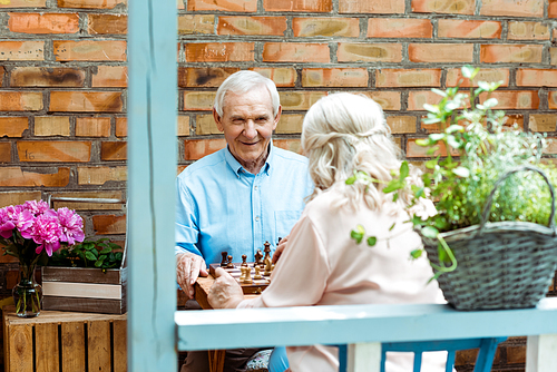 selective focus of happy senior man playing chess with wife