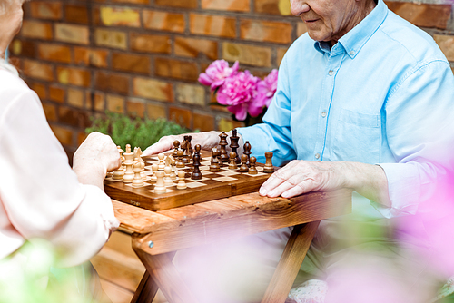 cropped view of retired couple playing chess on wooden table