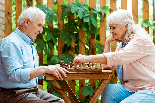 retired woman with grey hair playing chess with senior husband