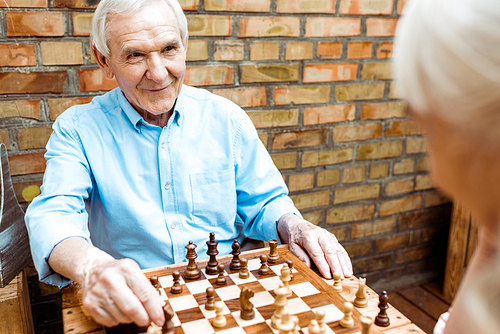 selective focus of cheerful retired man playing chess with senior wife