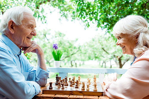 cheerful retired woman with grey hair playing chess with senior husband