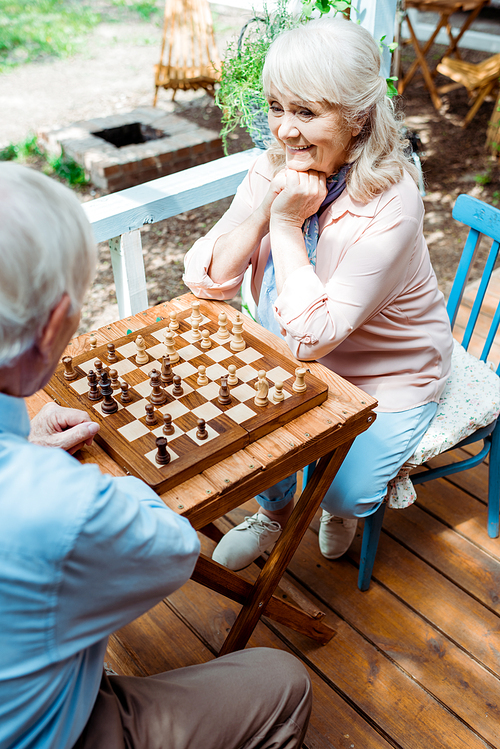 overhead view of cheerful retired woman playing chess with senior husband