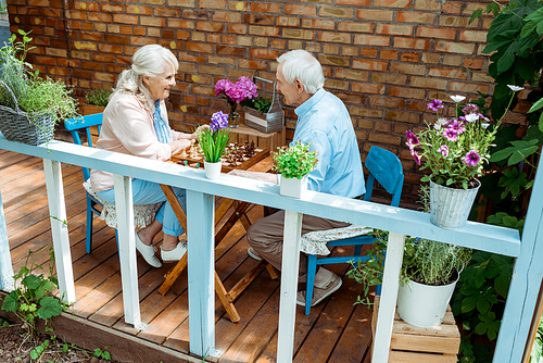 happy retired couple playing chess while sitting on terrace