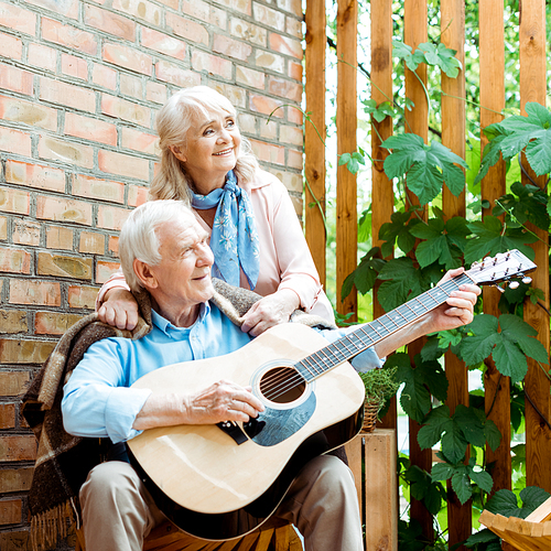 happy retired husband playing acoustic guitar near senior wife