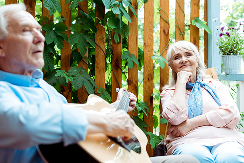 selective focus of retired woman listening while husband playing acoustic guitar