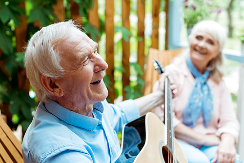 selective focus of happy retired husband playing acoustic guitar near senior wife