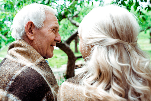 selective focus of smiling senior man in plaid blanket near wife