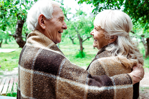 senior husband hugging happy retired wife in plaid blanket