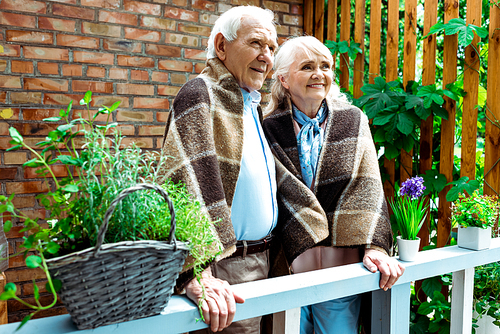 selective focus of happy senior wife and husband standing in plaid blankets near plants