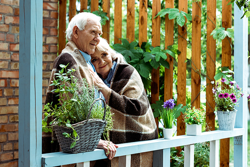 selective focus of happy senior woman in plaid blanket standing with husband on terrace