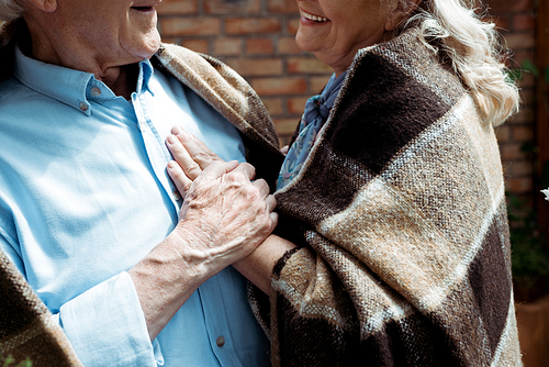 cropped view of happy retired woman touching senior husband in plaid blanket