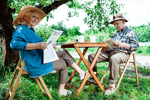 senior woman reading travel newspaper near husband with book