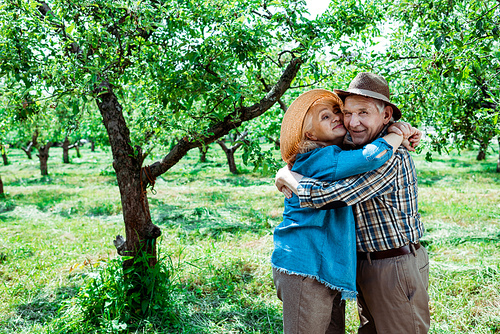 cheerful senior woman hugging happy retired husband in straw hat