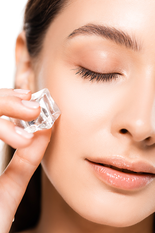 close up view of beautiful brunette young woman with perfect skin and closed eyes holding ice cube isolated on white