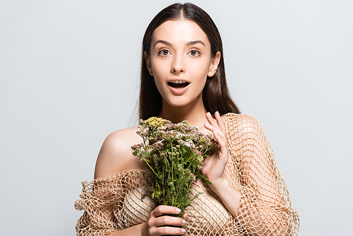 beautiful shocked woman in beige mesh with wildflowers looking away isolated on grey