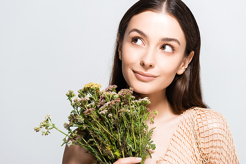 beautiful smiling woman in beige mesh with wildflowers looking away isolated on grey