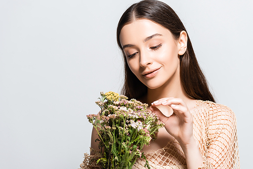 beautiful smiling woman in beige mesh looking at wildflowers isolated on grey