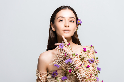 beautiful girl in mesh beige clothing with purple flowers touching face isolated on grey