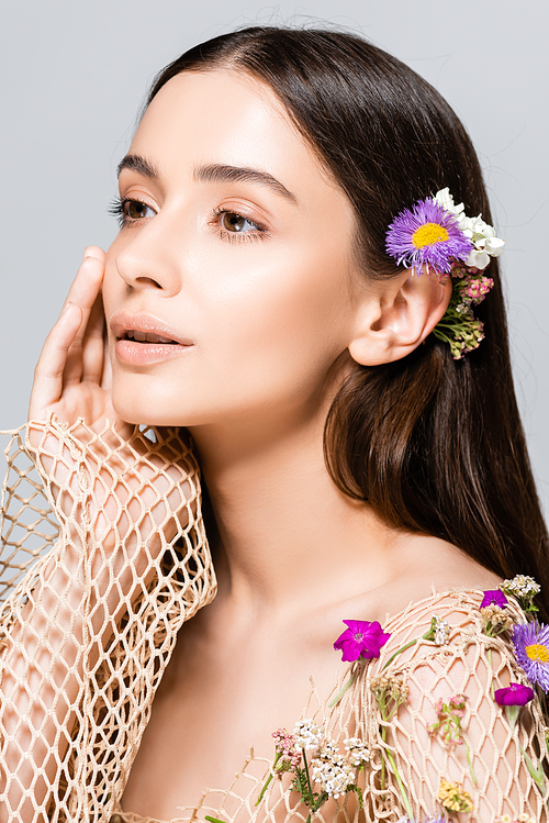 beautiful model in mesh beige clothing with purple flowers touching face isolated on grey