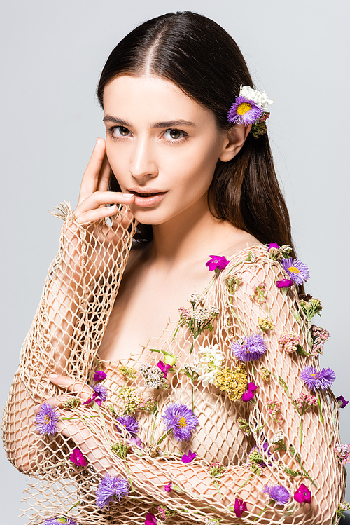 beautiful woman in mesh beige clothing with purple flowers touching lips isolated on grey