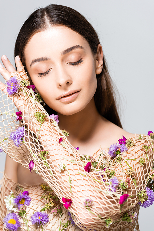 beautiful woman with closed eyes in mesh beige clothing with purple flowers posing isolated on grey