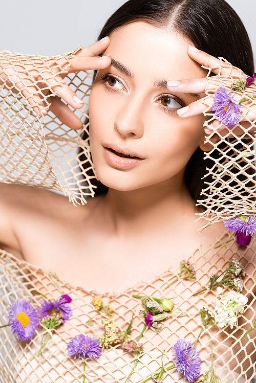 beautiful woman in mesh beige clothing with purple flowers posing isolated on grey