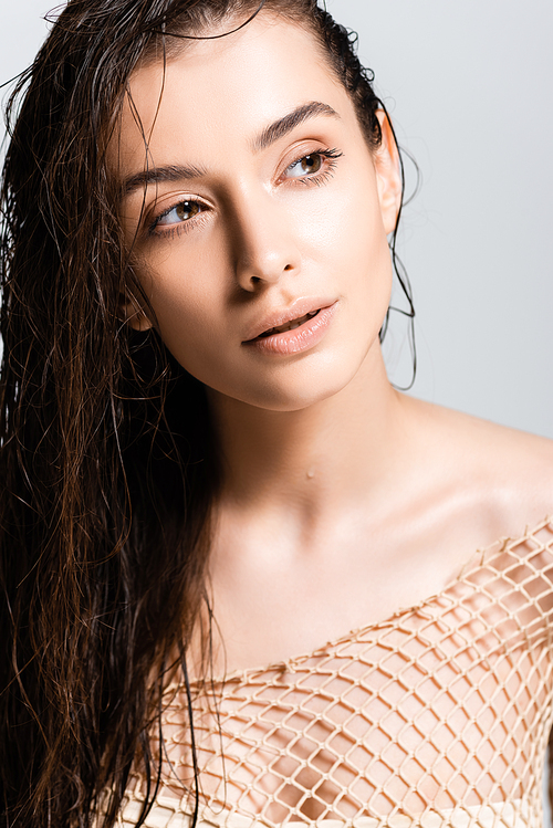 beautiful woman with wet hair in mesh beige clothing looking away isolated on grey