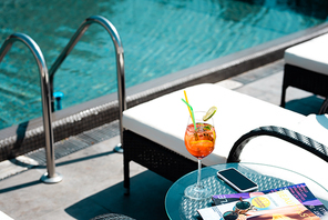 table with cocktail, magazines and sunglasses near swimming pool on resort