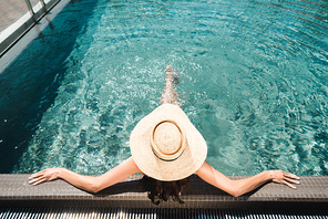 back view on woman in straw hat relaxing in swimming  pool