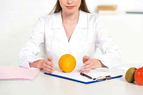 partial view of dietitian in white coat with fruits and vegetable at workplace