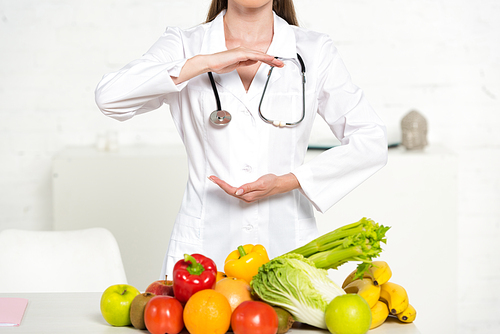 partial view of itian in white coat with stethoscope near fresh fruits and vegetables