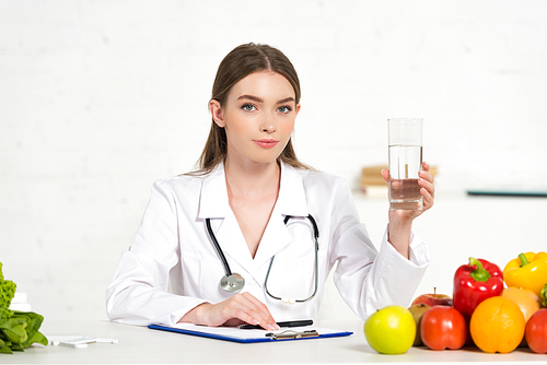 dietitian in white coat holding glass of water at workplace