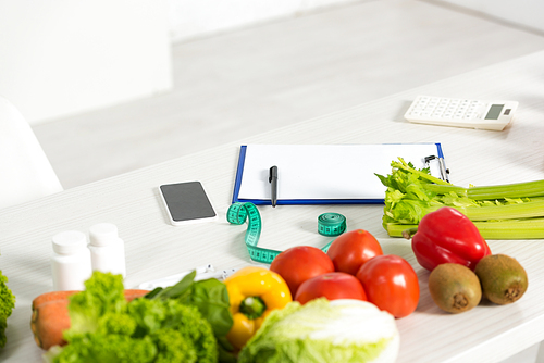 clipboard with pen, measure tape, smartphone with blank screen, calculator, medicine and fresh vegetables on table
