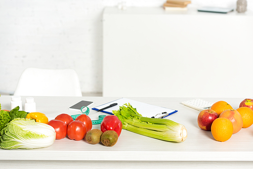 pills, smartphone with blank screen, clipboard with pen, fresh fruits and vegetables on table