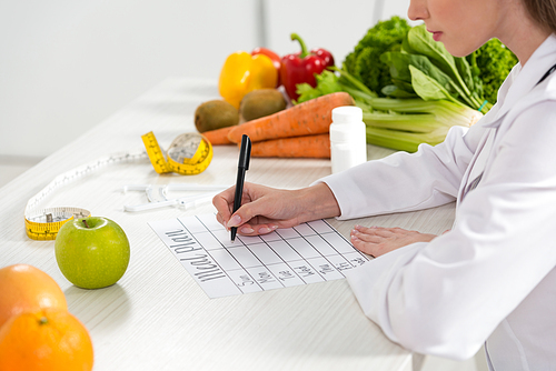 cropped view of dietitian writing in meal plan at workplace