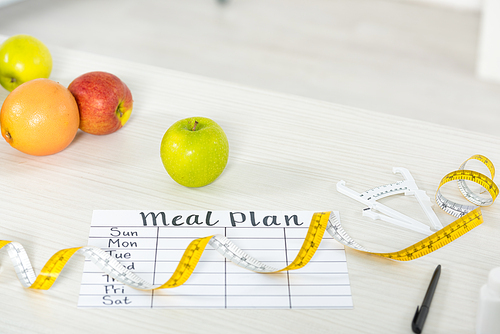 meal plan, measure tape, caliper, pen and fresh fruits on wooden surface