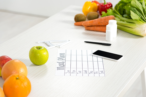 meal plan, smartphone with blank screen, pills, pen, caliper, fresh fruits and vegetables on table