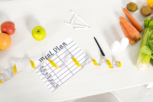 top view of meal plan, measure tape, pen, caliper, pills and fresh fruits and vegetables on table