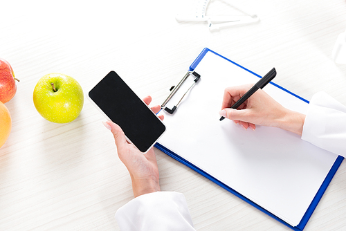 cropped view of dietitian holding smartphone with blank screen and writing in clipboard