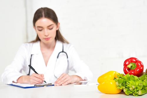 selective focus of dietitian in white coat writing in clipboard