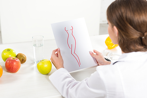 cropped view of dietitian in white coat holding paper with perfect body image at workplace