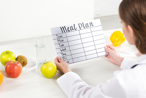 cropped view of dietitian in white coat holding meal plan at workplace