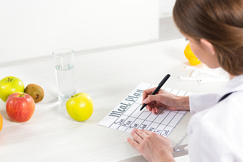 cropped view of dietitian writing meal plan at table