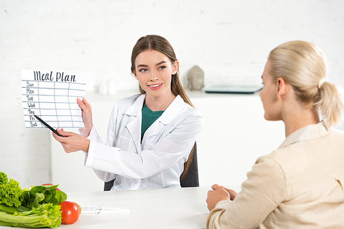 smiling dietitian in white coat holding meal plan and patient at table