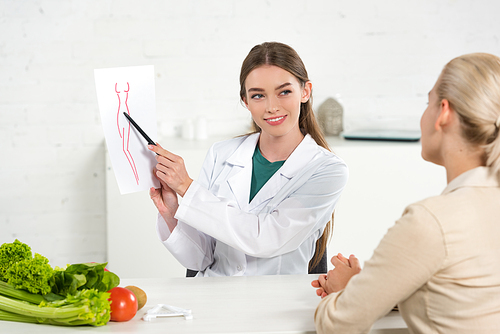 smiling dietitian in white coat showing paper with perfect body image to patient
