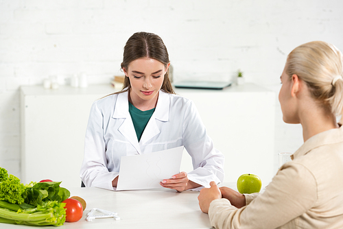 dietitian in white coat holding paper and patient at table