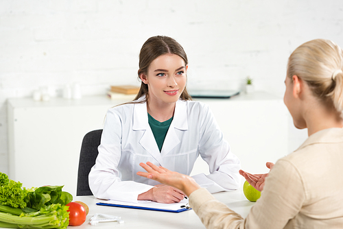 smiling dietitian in white coat looking at patient at table