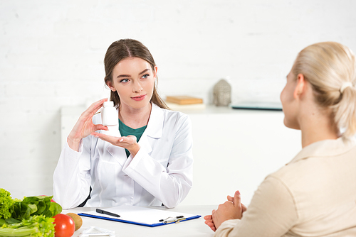 dietitian in white coat holding pills and patient at table